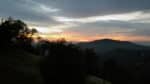 Yellow-to-coral sunset beneath gray clouds that darken a hilly landscape